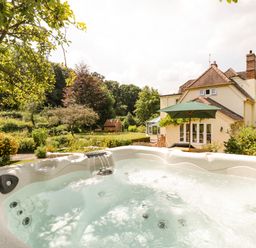 An outdoor hot tub with water jets in a garden with trees and a house in the background at Valley House in Devizes