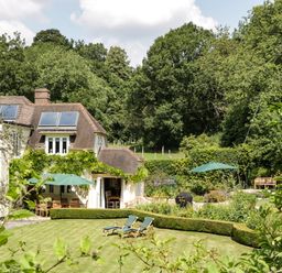 A garden with lounge chairs umbrellas and hedges next to a house with solar panels at Valley House in Devizes