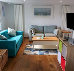 A living room with two sofas a wooden coffee table a wall-mounted TV and a storage unit with colorful bins at Furneaux Hatch in Churchstow