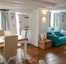 A dining area with a wooden table and beige chairs next to a blue sofa and wicker basket at Furneaux Hatch in Churchstow