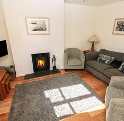 A living room with a fireplace armchairs a sofa cushions a lamp television and a rug at Oysterbank Cottage in Llangwm Pembrokeshire