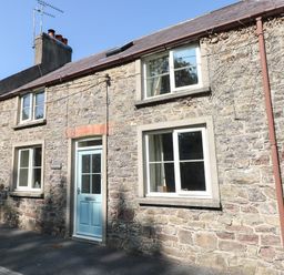 Stone cottage with blue door and multiple windows on a street at Oysterbank Cottage in Llangwm Pembrokeshire