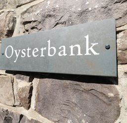 A metal sign with the word Oysterbank mounted on a stone wall at Oysterbank Cottage in Llangwm Pembrokeshire