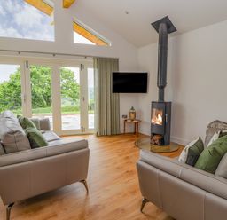 A living room with two sofas a wood burning stove a wall mounted television and large windows at Pen Bryn in Cyffylliog near Ruthin