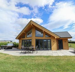 A wooden house with large glass windows patio furniture and a hot tub on a tiled patio with grass in front at Pen Bryn in Cyffylliog near Ruthin