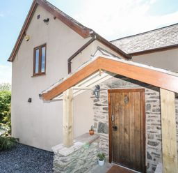 The exterior of a house with a wooden door set in a stone wall and a small porch roof supported by wooden beams at Hafotty Gelynen in Maerdy near Corwen