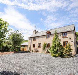 A gravel driveway with trees and shrubs around a two-story house under a blue sky at Hafotty Gelynen Maerdy near Corwen