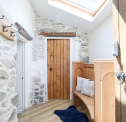 A hallway with stone walls wooden doors a wooden bench with cushions a coat rack and a skylight at Hafotty Gelynen in Maerdy near Corwen