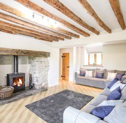 A living room with a fireplace wooden beams on the ceiling two sofas and a rug on the floor at Hafotty Gelynen Maerdy near Corwen