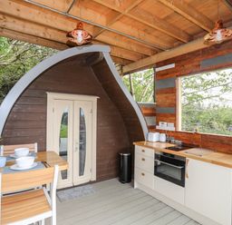 A kitchen area with wooden countertops stools and a dining table with dishes at Woodland Pod Maerdy near Corwen