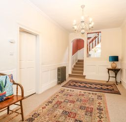 A hallway with stairs rugs a wooden chair with a cushion a small table with a lamp and a chandelier at Enterprise House in Bury St Edmunds