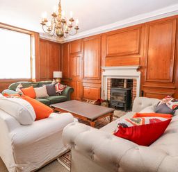 A living room with wooden paneling a chandelier sofas with cushions a coffee table and a fireplace at Enterprise House in Bury St Edmunds