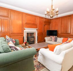 A living room with wood panel walls a green sofa a white sofa a fireplace a wooden coffee table and a chandelier at Enterprise House in Bury St Edmunds