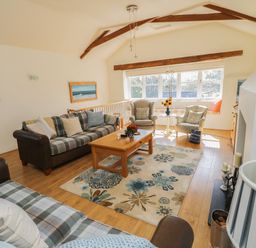 A living room with sofas, armchairs, a wooden coffee table, floral rug, and large windows at Crosscombe Barn in Loddiswell