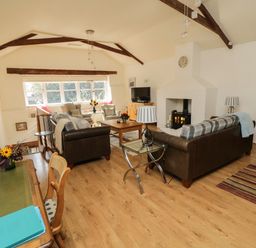 A living room with sofas, armchairs, a coffee table, a fireplace, a television, and a dining table with chairs at Crosscombe Barn in Loddiswell