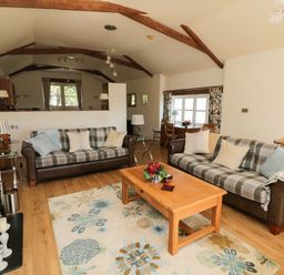 A living room with two plaid sofas a wooden coffee table and a dining table near a window at Crosscombe Barn in Loddiswell