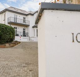 The exterior of a white house with balconies and a driveway with a white wall showing the number 10 Riviera Heights Paignton