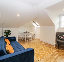 A room with a blue sofa with orange cushions a yellow rug a dining table with white chairs a grey armchair and a window with blinds at Riviera Heights in Paignton