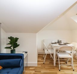 A small dining area with a white table and four white chairs beside a blue sofa with an orange pillow and a plant on a side table at Riviera Heights Paignton