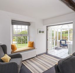 A sitting room with striped armchair cushions window seat and doorway leading to a conservatory at Greenstyles in Bowness-On-Windermere