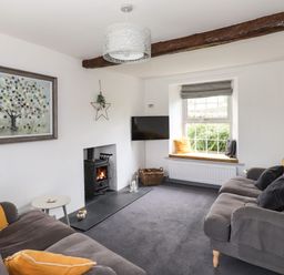 A living room with grey sofas yellow cushions a wood stove and window seat at Greenstyles in Bowness-On-Windermere