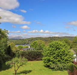 A garden with trees and grass overlooking a lake and hills at Greenstyles in Bowness-On-Windermere