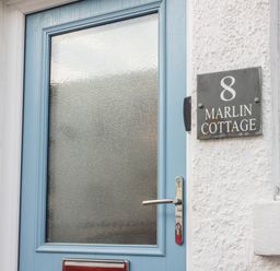 A blue front door with frosted glass and a house sign reading 8 Marlin Cottage in Conwy
