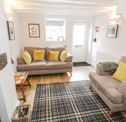 A living room with two beige sofas and yellow cushions a checkered rug a wooden side table and wall art at Marlin Cottage in Conwy