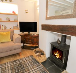 A living room with an armchair a television on a wooden cabinet a fireplace with a wood stove and a basket with firewood at Marlin Cottage in Conwy