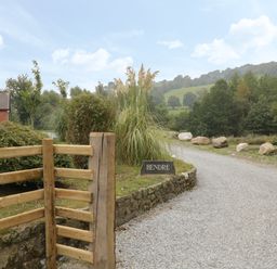 A gravel driveway leading to a house with wooden fencing and a stone sign that says Hendre at Penybontfawr