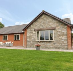 A house with stone and brick exterior with windows a garage door a patio with outdoor seating and potted plants at Hendre in Penybontfawr