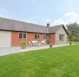 A bungalow with a garage and outdoor seating on a patio in a garden at Hendre in Penybontfawr