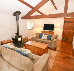 A living room with two sofas a wood stove a wooden coffee table a television and wooden beams at Nant Bach in Boduan near Nefyn