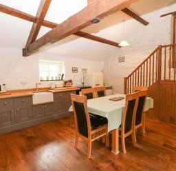 A kitchen with a dining table and chairs wooden beams on the ceiling and stairs leading to a loft at Nant Bach Boduan near Nefyn