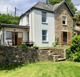 A two-story house with stone and white walls with a lawn and stone wall in front at Wottonsbury in Ilsington