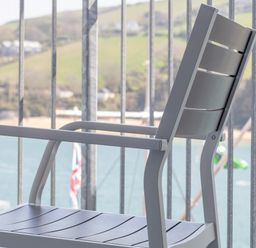 A gray metal chair on a balcony overlooking water and hills at 32 The Salcombe in Salcombe