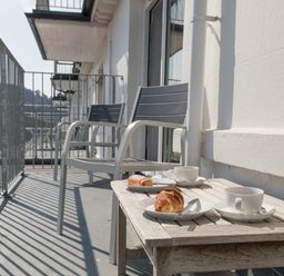 A balcony with two chairs a wooden table with croissants and cups at 32 The Salcombe in Salcombe