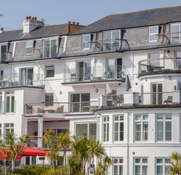 White multi-story building with balconies and outdoor furniture and palm trees in front at 32 The Salcombe in Salcombe