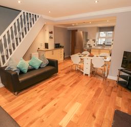 An open-plan living room and kitchen with a staircase a sofa with cushions a dining table with chairs a refrigerator and a television at Annest in Bethesda