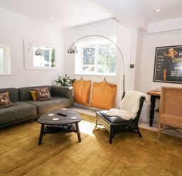 A living room with a grey sofa, coffee table, two orange bean bags, an accent chair, desk with a wicker chair, and a framed poster at Kub House in Wigginton Hertfordshire