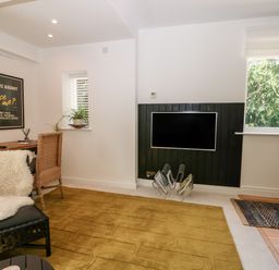 A room with a mounted flat screen tv rattan chair a wooden desk with plants and a black framed poster on the wall at Kub House in Wigginton Hertfordshire