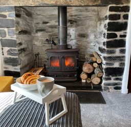 A living room with a wood burning stove firewood and a tray with a cup and pastries at 7 Castle Terrace Dolwyddelan