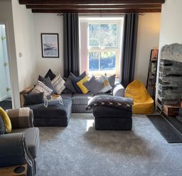 A living room with a sofa and cushions next to a stone fireplace with a fire at 7 Castle Terrace in Dolwyddelan