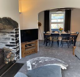 A living room with a wood burning stove television and a dining table set for six at 7 Castle Terrace in Dolwyddelan