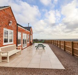 A brick house with white bench windows doors and wooden fence on tiled patio at Border View Lodge in Llandrinio