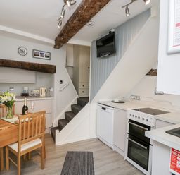 A kitchen with wooden dining table and chairs a built in oven dishwasher countertop sink and stairs at Cobblers Cottage in Upton Upon Severn