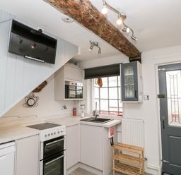 A kitchen with a stove dishwasher sink microwave wall mounted tv and wooden shelf at Cobblers Cottage in Upton Upon Severn