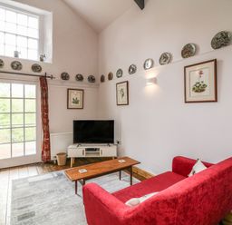 A sitting room with a red sofa wooden coffee table TV on a stand decorative plates on the walls at Wisteria Cottage in Marldon