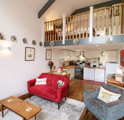 A living room with red and grey armchairs a wooden coffee table and an open kitchen with wood floors at Wisteria Cottage in Marldon