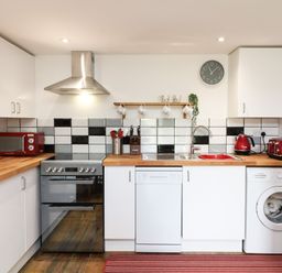 A kitchen with white cabinets wooden countertops and black white and gray tiled backsplash at Wisteria Cottage in Marldon